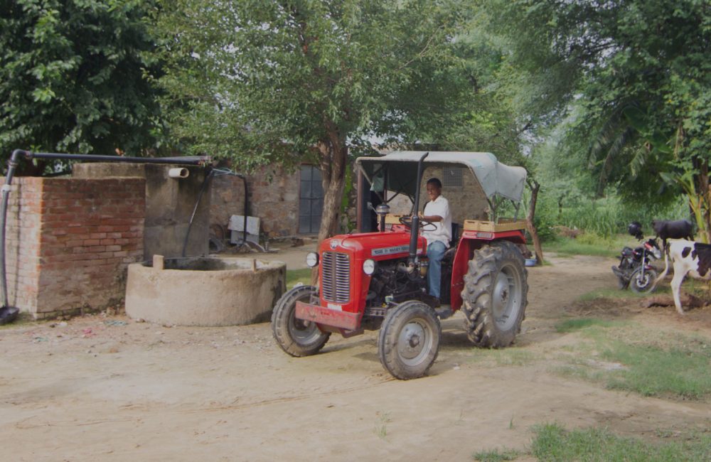 Man drives a red tractor past some trees