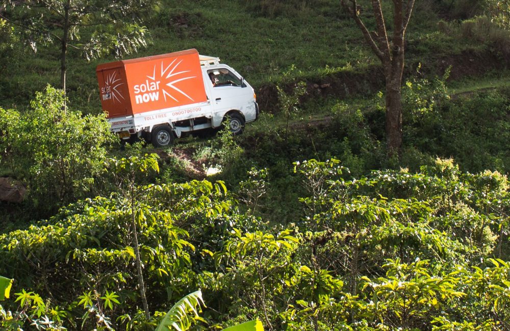 An orange truck drives through a green forest opening